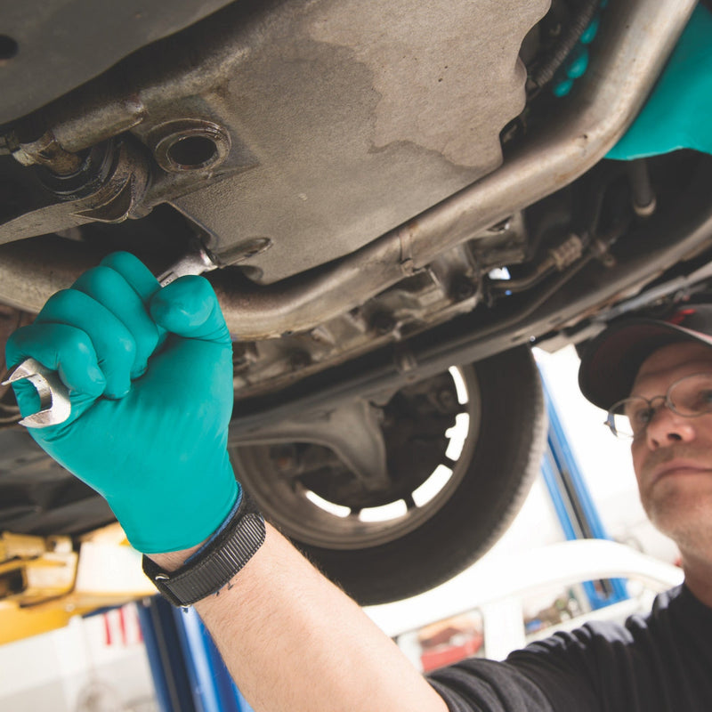 Person working on a vehicle undercarriage with a wrench, wearing green gloves.