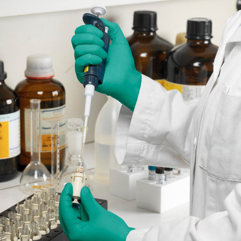 Person in a lab setting using a pipette with laboratory equipment and chemicals in the background | www.theglovestore.co.uk